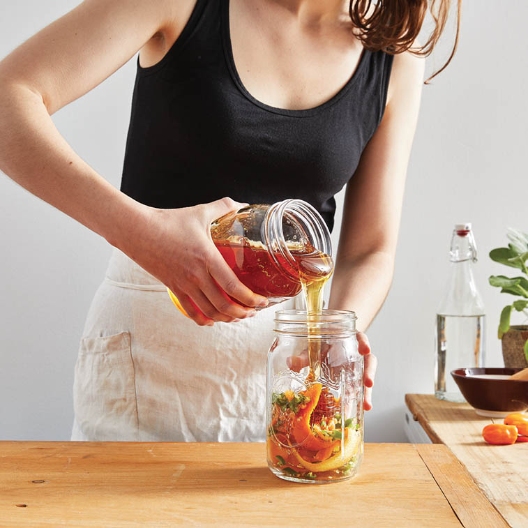 Pouring the honey into a jar with orange peels and diced peppers.