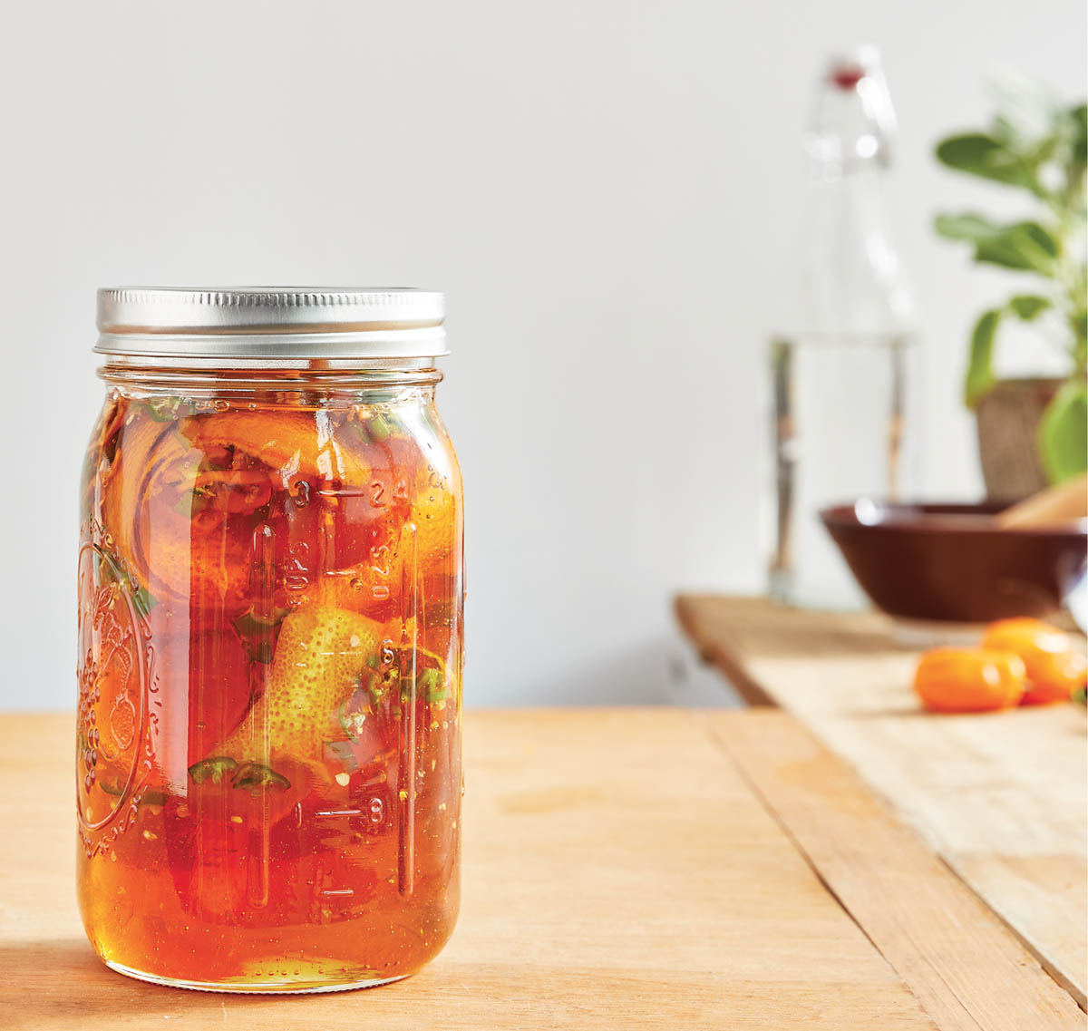 A jar of honey with orange peels and peppers.