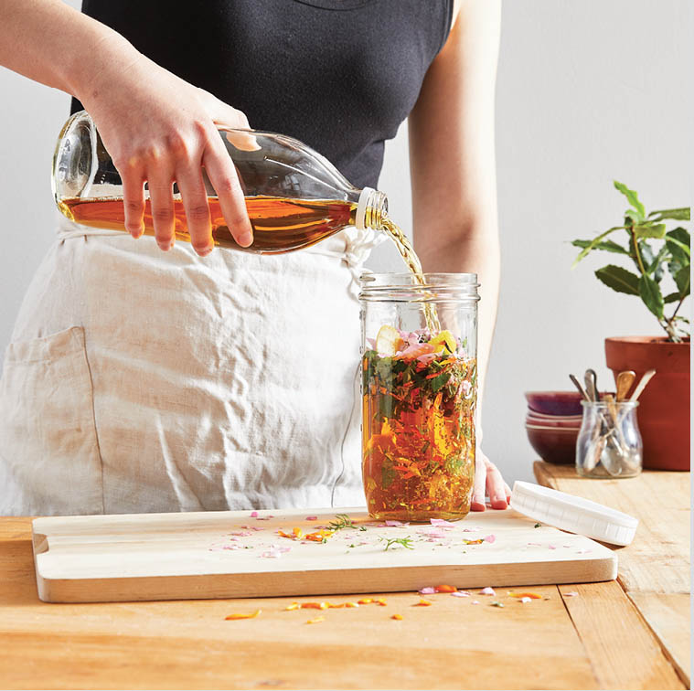 Pouring apple cider vinegar into the jar of herbs and flowers.