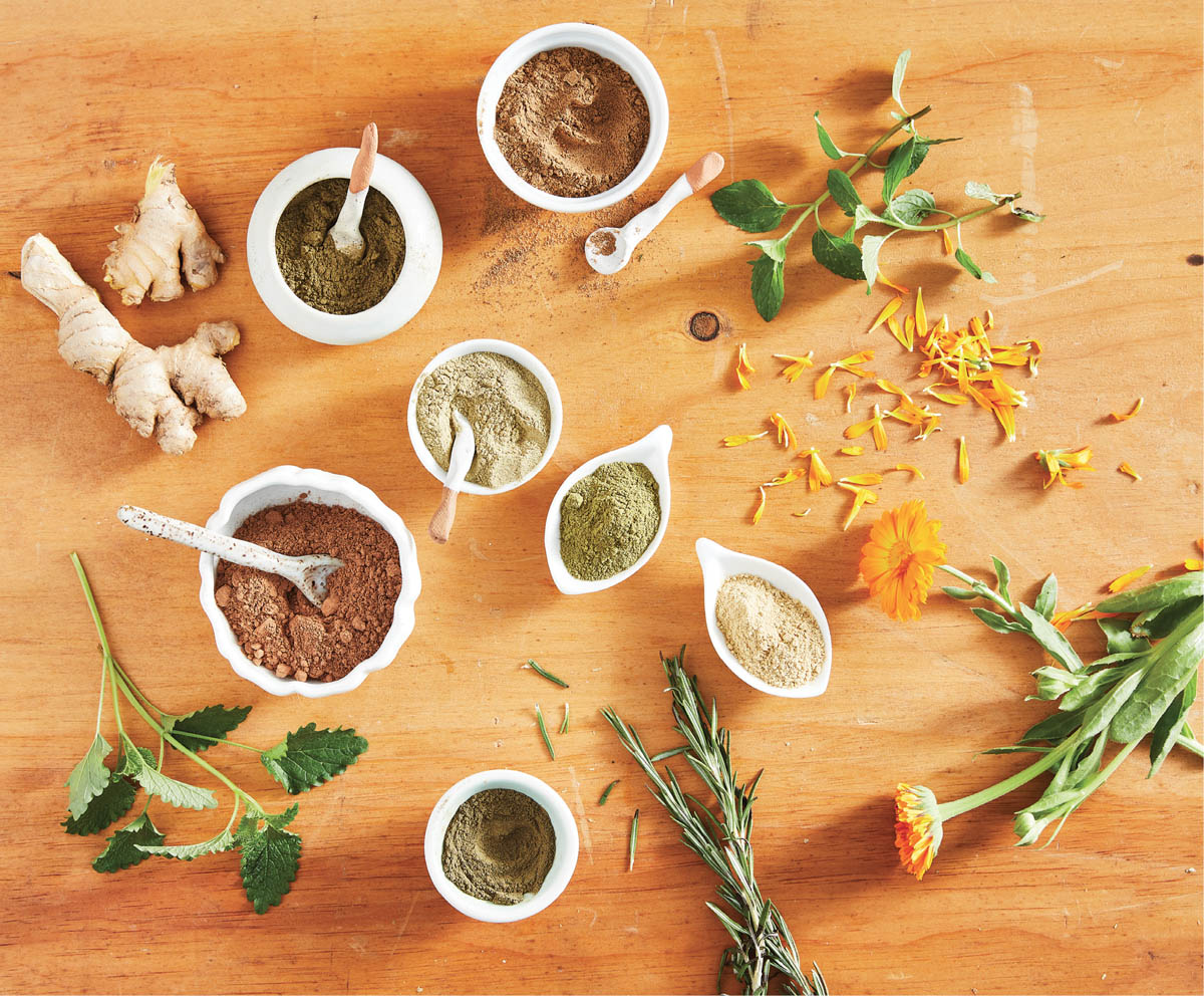 A spread of powders, freshly picked herbs, flowers, and ginger root.