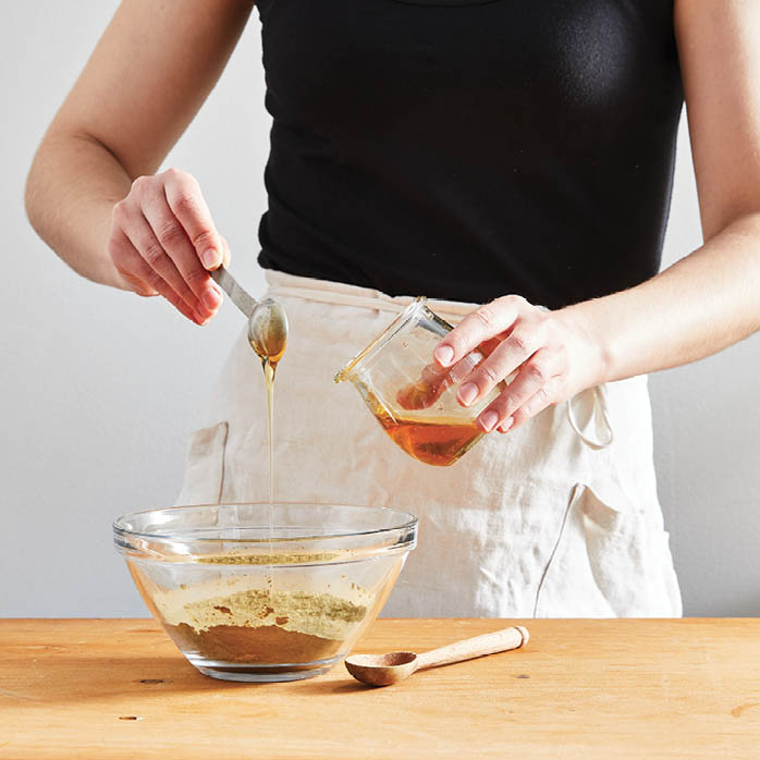 Measuring out teaspoons of honey into the powdered ingredients.