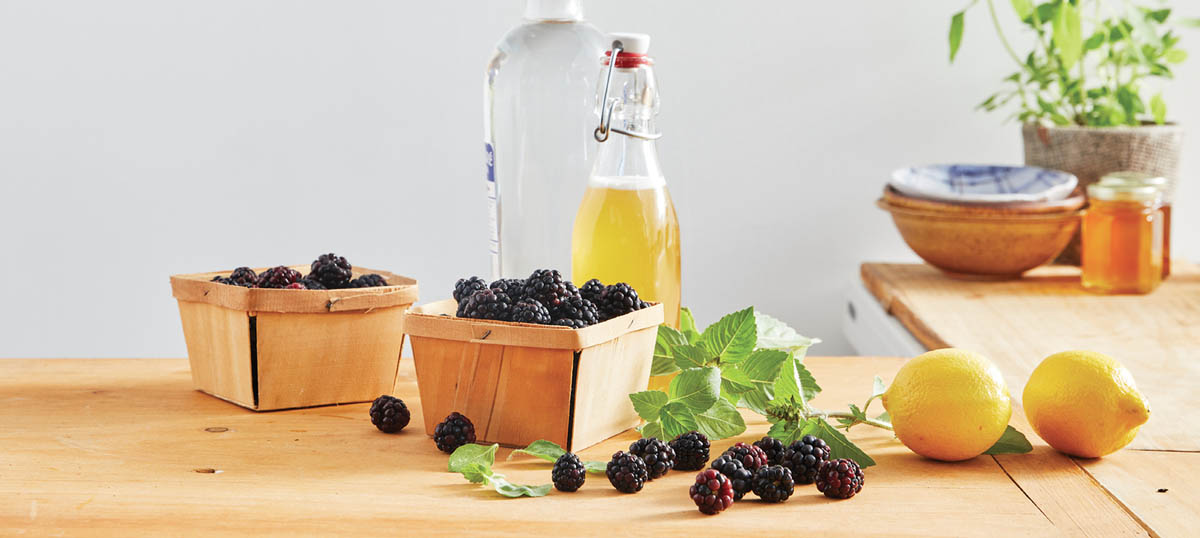 A spread of fresh herbs, lemons, raspberries, and a bottle of vinegar.