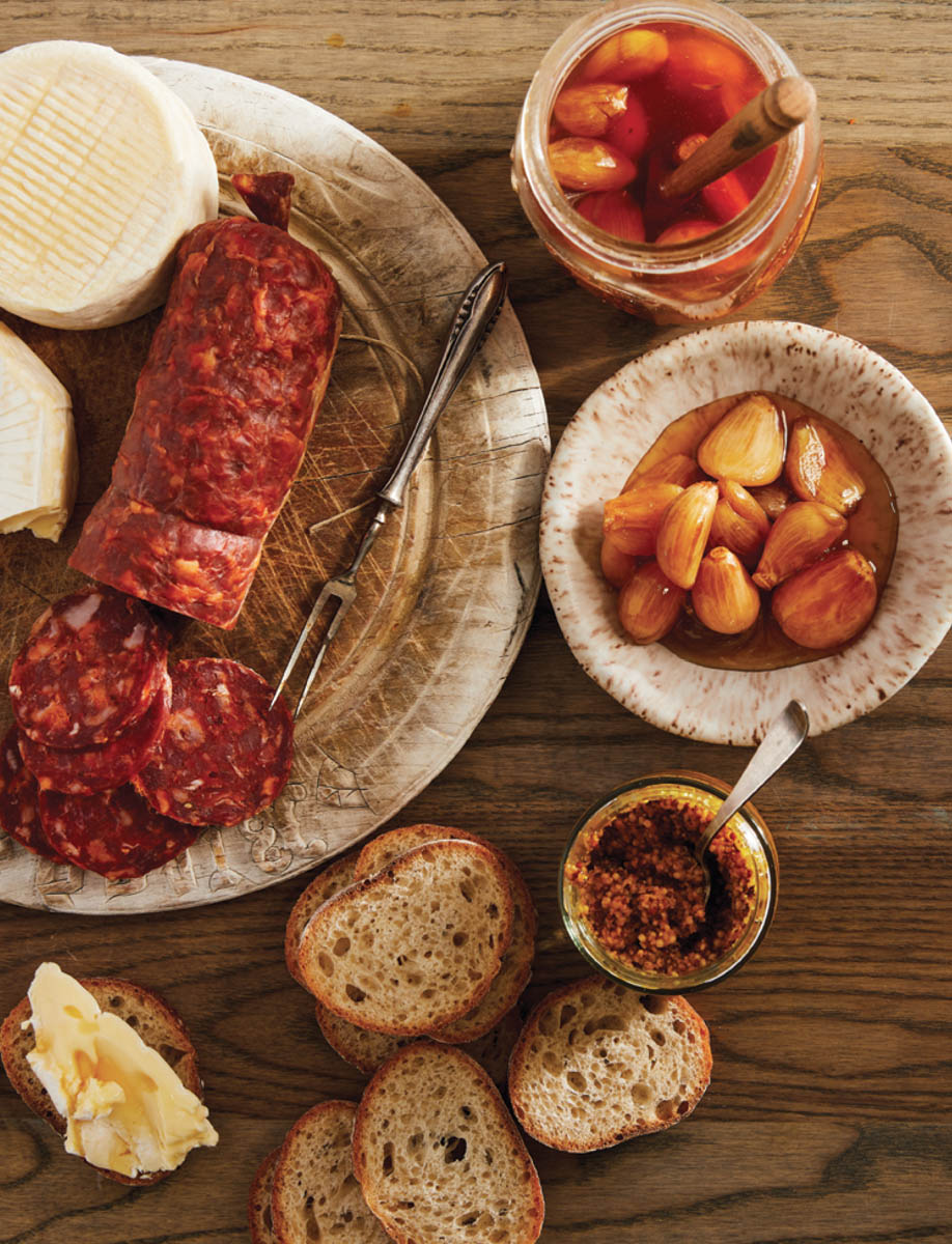 A spread of food and fermented items with honey, including garlic, bread, mustard, and sausage.