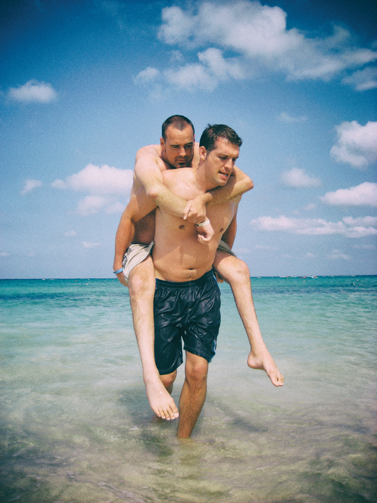 Patrick carries Justin piggy-back in shallow ocean water.