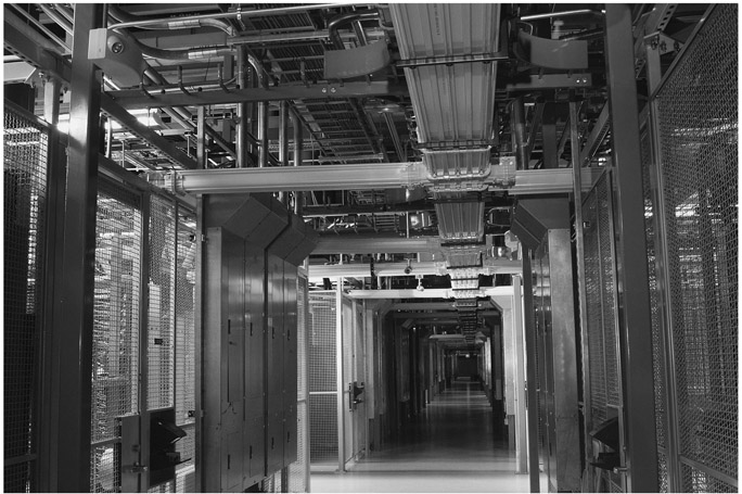 Figure 3.2 The inside of the Equinix Internet Peering Point in Ashburn, Virginia. Behind the cages are the servers that are run by major companies like Amazon, EA Games, Verizon and Google. The yellow trays along the aisles hold the fiber-optic cables running between these server cages. © 2011 Equinix, Inc. All rights reserved. The Equinix logo is a trademark of Equinix, Inc.