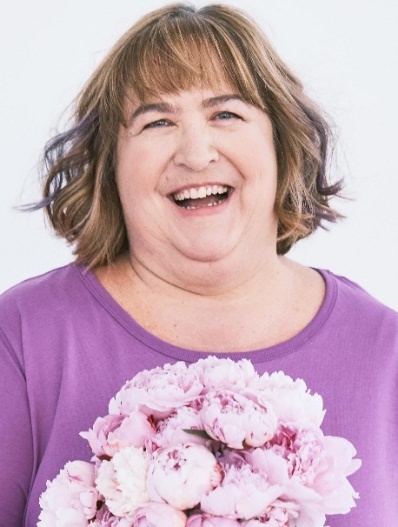 A person holding a donut with white and pink flowers Description automatically generated