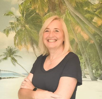 A person smiling with palm trees in the background  Description automatically generated with low confidence