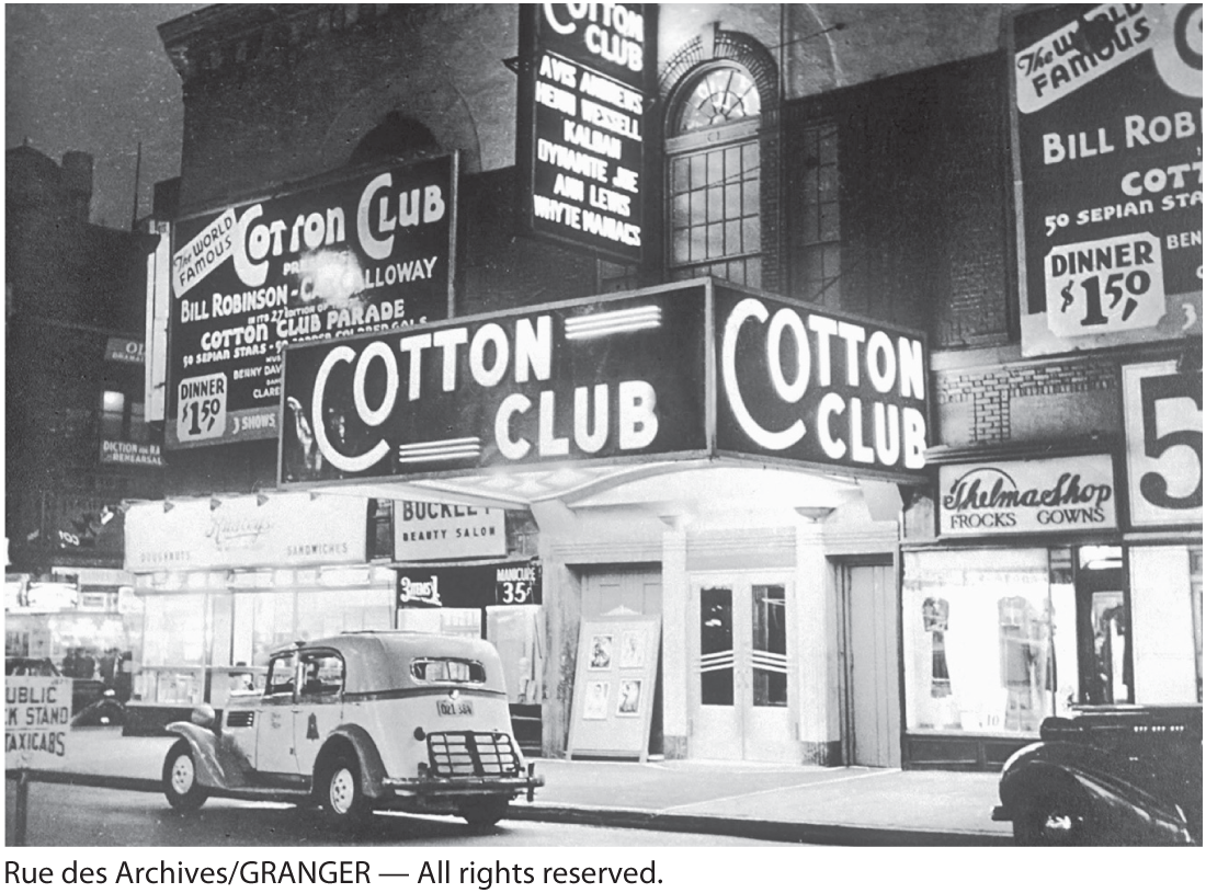 A photo shows a club named ‘Cotton Club’ situated on the side of a road; two old cars are parked on the pavement in front of the club.