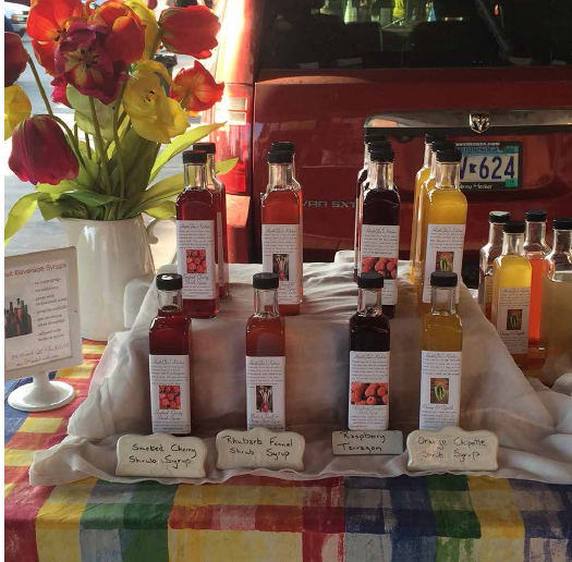 HeathGlen’s Farm & Kitchen syrups displayed at a farmers’ market stand. COURTESY OF HEATHGLEN’S FARM & KITCHEN