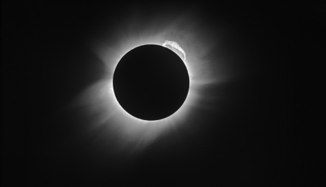 Start of image description, An image of the total solar eclipse captured by Arthur Eddington and Edwin Cottingham from Príncipe, off the coast of Equatorial Guinea in west Africa, in May 1919. The pitch black moon is surrounded by a solar corona., end of image description