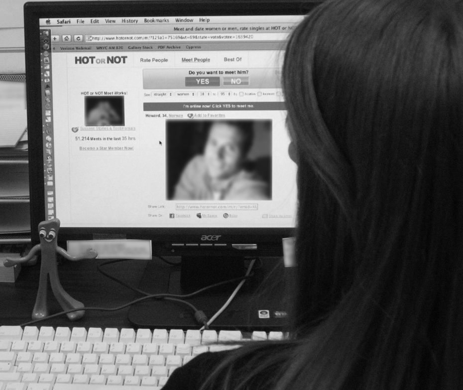 A woman looking at a computer screen with the website titled Hot or Not displayed.