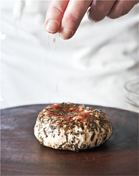 Sprinkling spices onto a round of cheese