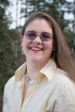 Photo of author Christiane Joy Allison wearing a yellow shirt, silver necklace, and colored glasses. 