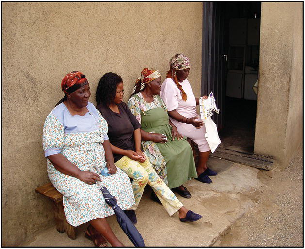 Photo of four African women sitting on a bench by an open door.