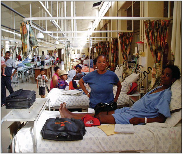 Photo of a hospital ward with patients and their visitors.