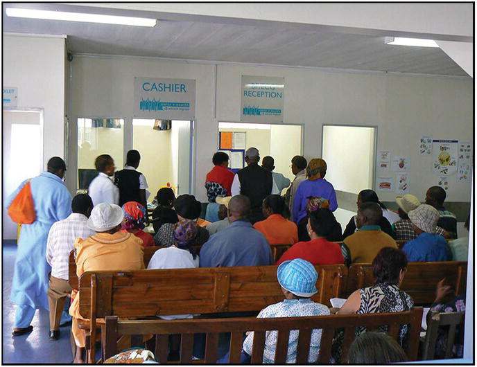 Photo of the waiting area filled with African men and women sitting in queue at the Cashier and BP/ECG Reception windows.