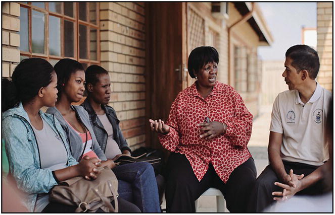 Photo of an African woman talking to a Caucasian man on the right while three African women on the left listen.