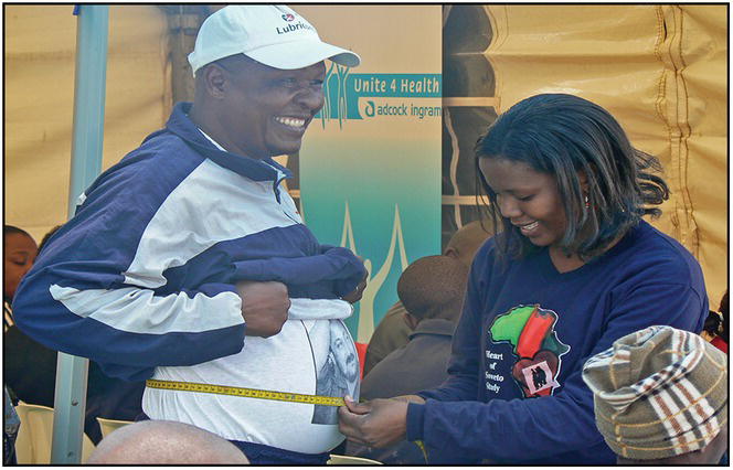 Photo of an African woman measuring a man's belly with a tape measure.