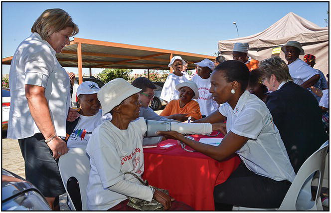 Photo of an African woman taking the blood pressure of an elderly woman during a medical mission.