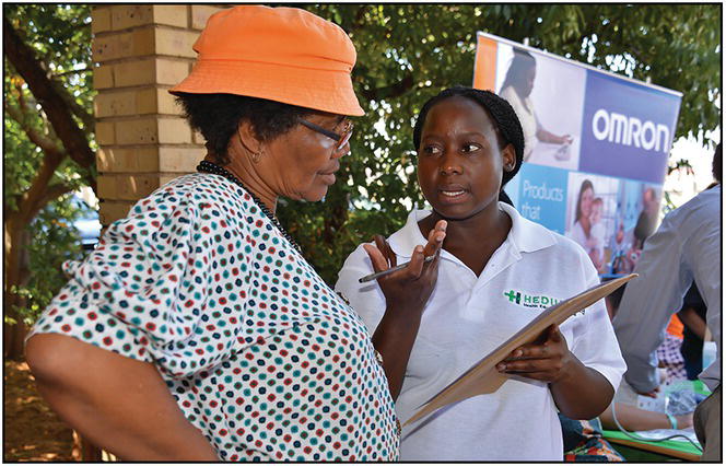 Photo of an elderly African woman listening to a younger African woman explaining with hand gestures while holding a clipboard.