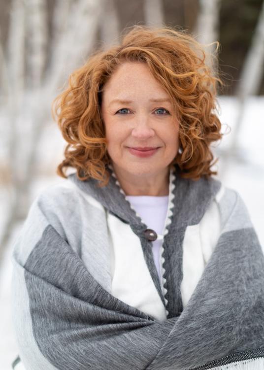 Author photo - red haired woman wearing a gray and white sweater stands in a wintery birch forest.