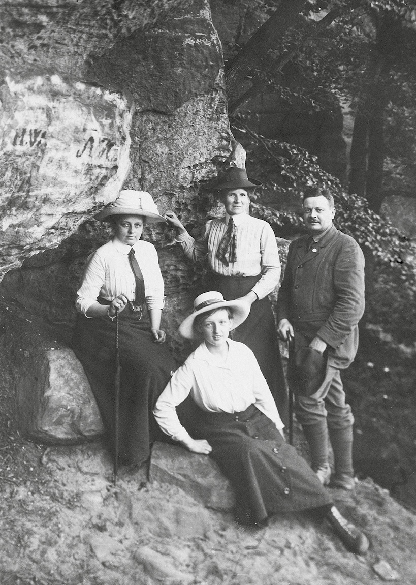 Foto von einem Ausflug: In der Bildmitte Kästners Mutter vor einer Felswand stehend, vor ihr sitzen seine Kusine Dora Augustin und zwei unbekannte Personen, alle in Wanderkleidung.