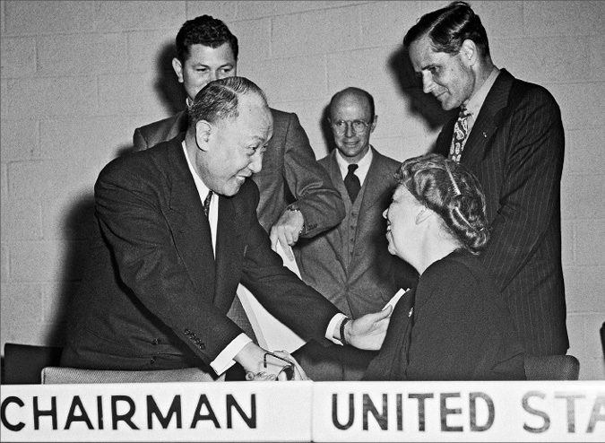 Dr. P.C. Chang shakes Eleanor’s hand as three men in suits look on.