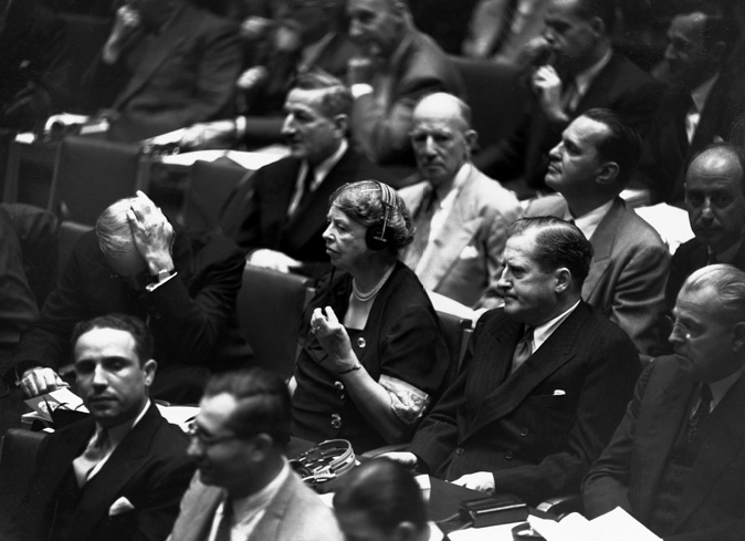 Seated in the audience, Eleanor listens intently with headphones, surrounded by stern-faced men.