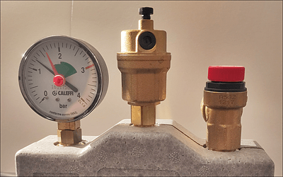 Druckmesser, automatisches Entlüftungsventil und Überdruckventil. Der
Wasserdruck im Heizungssystem (schwarzer Zeiger) ist zu klein. Er ist niedriger als der Referenzdruck (roter Zeiger). Es muss Wasser nachgefüllt werden.