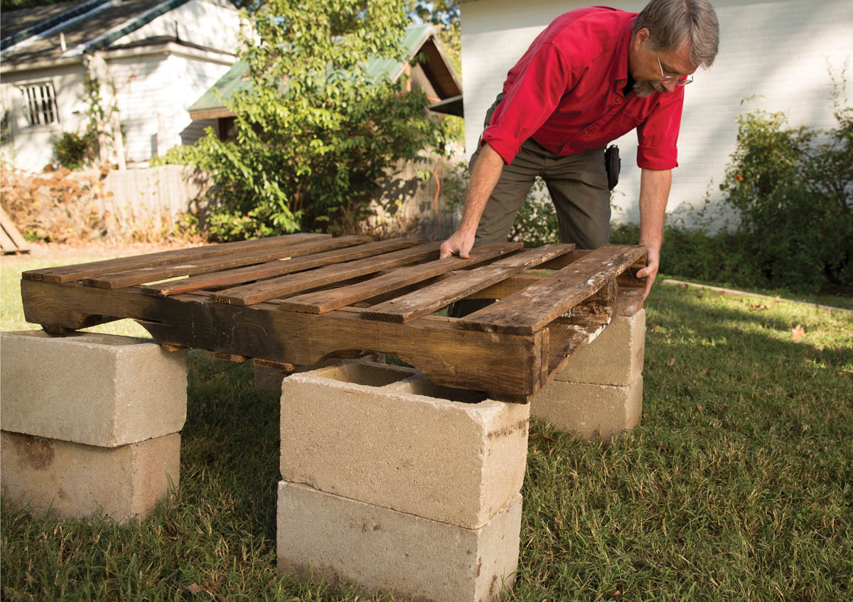 Placing a wood pallet on the cinder blocks.