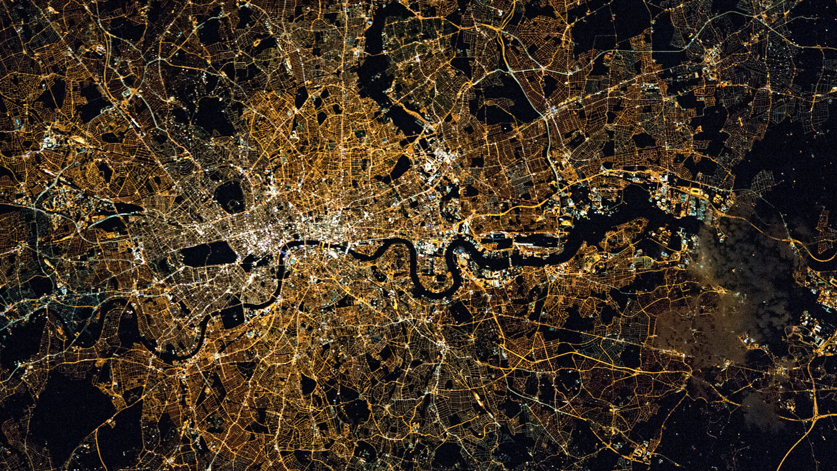 From the International Space Station, London shows up brightly at night, with the dark waters of the River Thames meandering through the city. Dark patches are open spaces, such as parks, and the street lighting changes from orange in the suburbs to white in the West End and City. © NASA / ISS Expedition 45 crew.