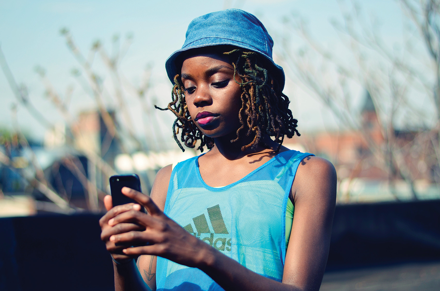 Photo of Zahra Siddiqui, a young black woman, wearing a hat and Adidas sport shirt and looking at her phone.