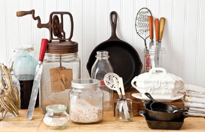 A collection of antique kitchen tools, including cast iron skillets and mason jars, arranged artfully on a wooden counter