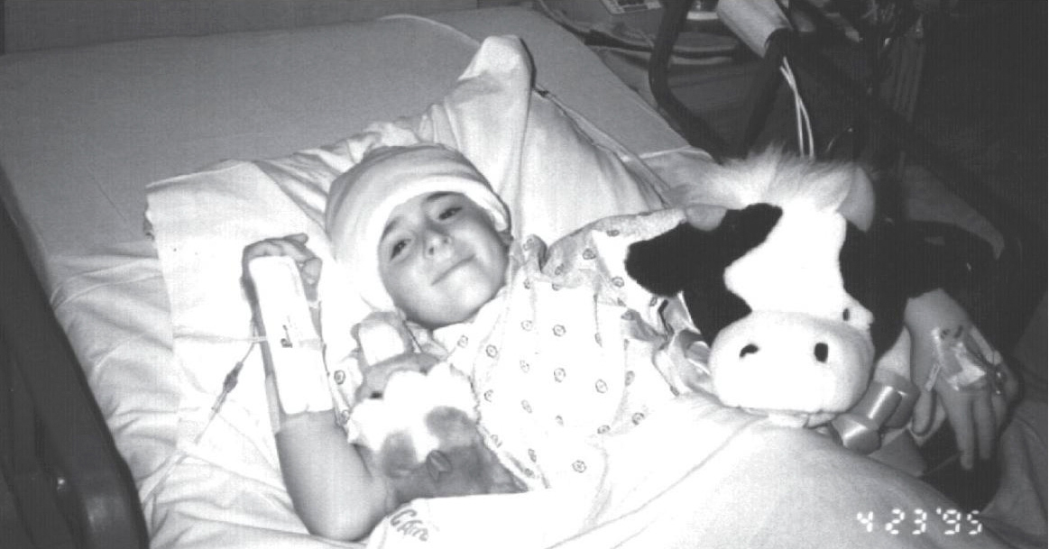 Andrew smiling at the camera while lying in his hospital bed, his head bandaged.