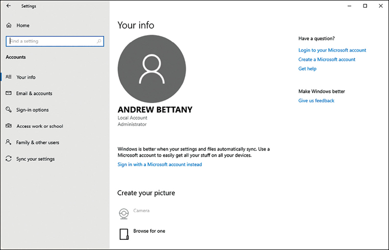 A screenshot shows the Settings app with the Your Info page displayed. Along the left is a list of items under accounts, including Your Info, Email And Accounts, Sign-In Options, Access Work Or School, Family And Other Users, and Sync Your Settings. In the center of the page is a large user icon with Andrew Bettany, Local account, and Administrator underneath. Beneath the Andrew Bettany icon is Sign In With A Microsoft Account Instead link.