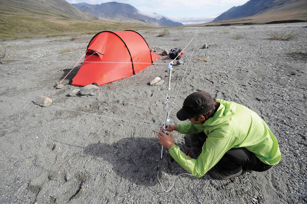 Photograph of camper setting up electric fence around his tent.