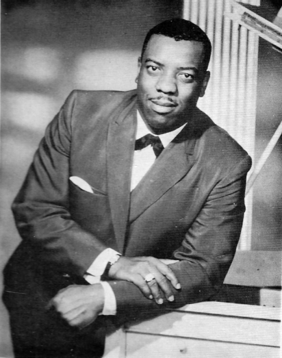 A photo of Reverend James Cleveland standing next to a table, with one arm resting on the table.