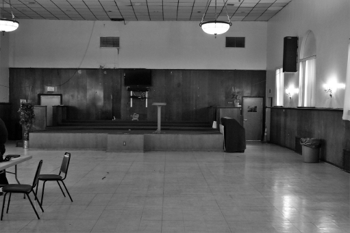 A photo of the interior of the Adventist Church in Newark. The space in front of the altar is vacant, except for a set of table and chairs on the left.