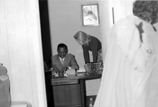 A photo of Doris Duke standing and talking to Reverend Lawrence Roberts, who sits at his desk.