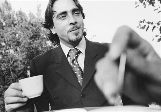 A dashing young man in a suit drinking coffee in a vineyard