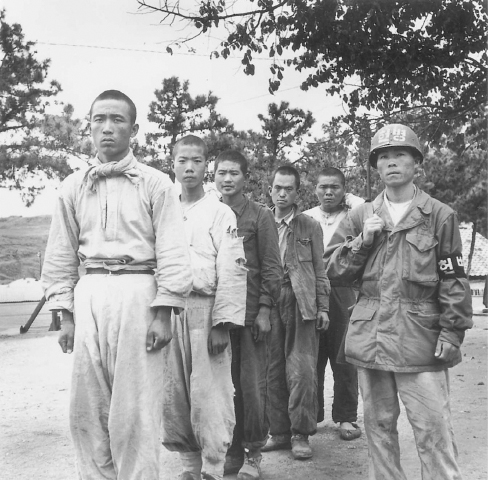 Prisoners guarded by a South Korean soldier wait to be taken to a POW camp near Inchon in October 1950. (UN Photo 32240)