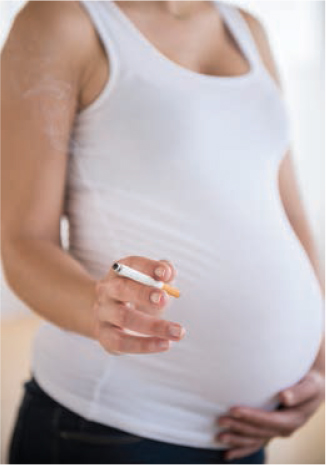 Photo of the midsection of a pregnant woman who is holding a lit cigarette.