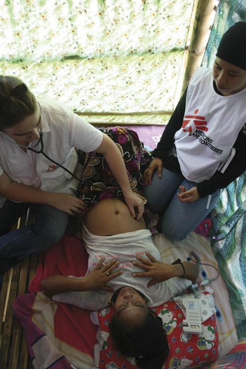 Photo of a baby being examined by a doctor, who is listening to the child’s stomach, while a family member looks on.