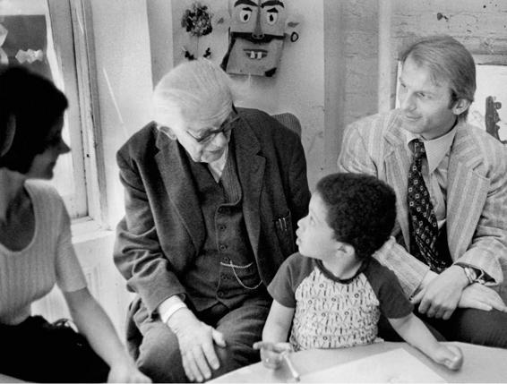 Photo of Piaget interviewing a child while two other adults, probably his parents, look on.