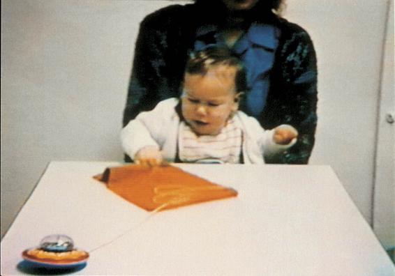 Photo of one-year-old pulling a cloth toward itself to gain access to a string attached to a toy. The string is drawn along with the cloth.