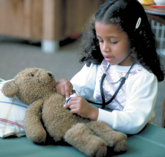 Photo of a little girl in the present day, dressed as a doctor and giving her teddy bear a physical exam.