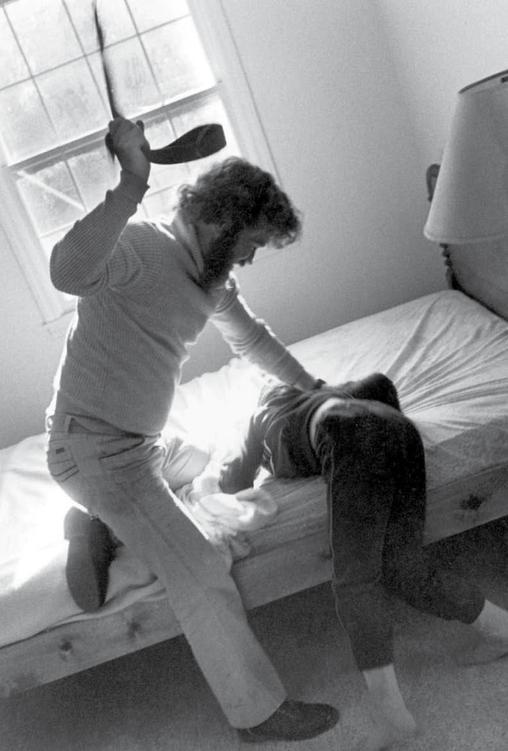 Photo of an adult holding a child down and using an object to spank her.