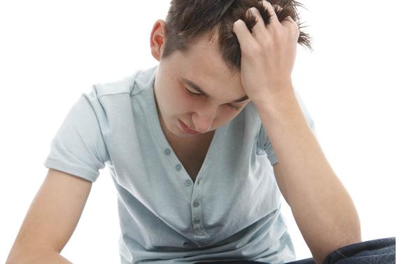 Photo of an adolescent appearing very stressed. He is clutching his hair and his posture is tense.