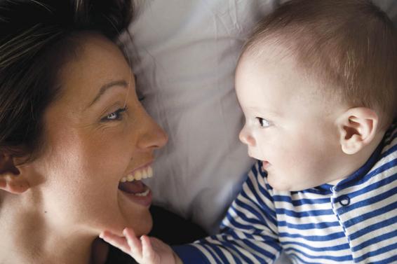 Photo of mother and baby interacting. Both smiling and making eye contact.