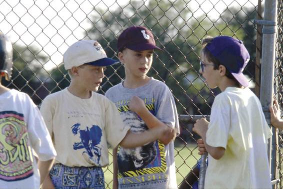 Three or four softball players standing on the field discuss the rules before a game.